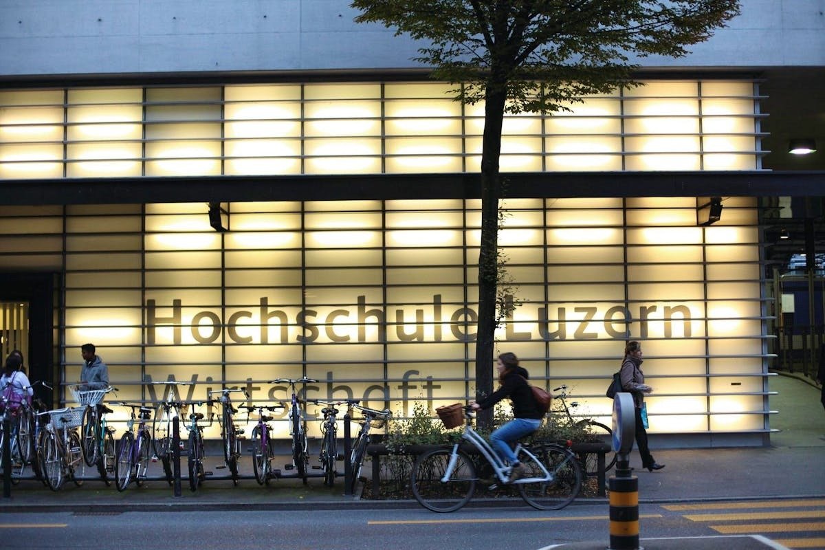 Hochschule Luzern – Wirtschaft building at dusk, with cyclists passing in front